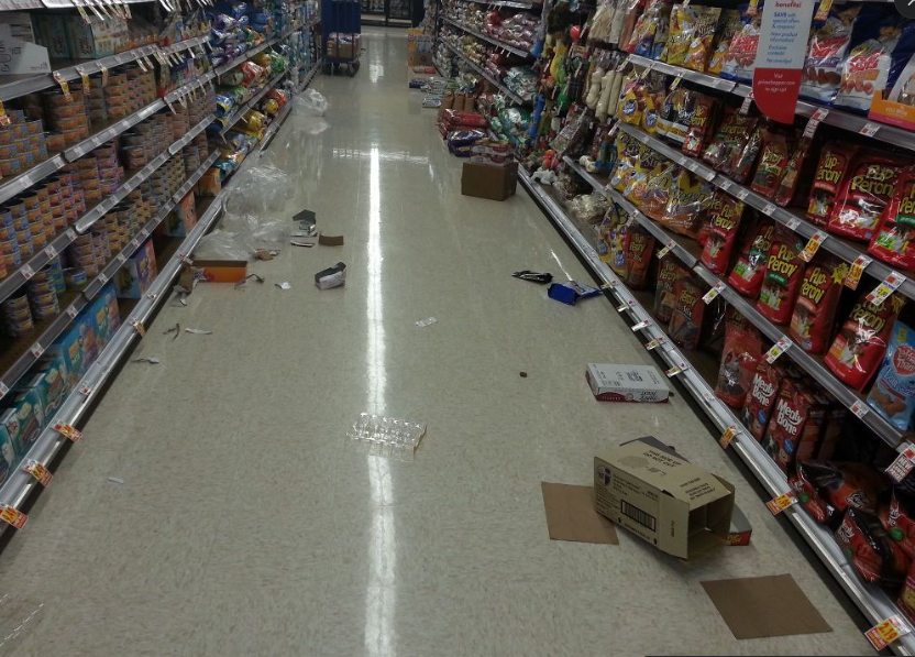Corredor de supermercado com caixas abertas, plástico e resíduos deixados no chão durante o horário de venda
