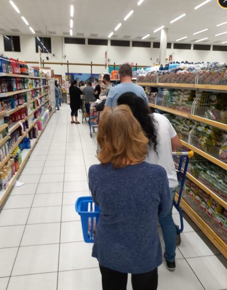 Clientes esperando em fila no corredor de checkout de um supermercado