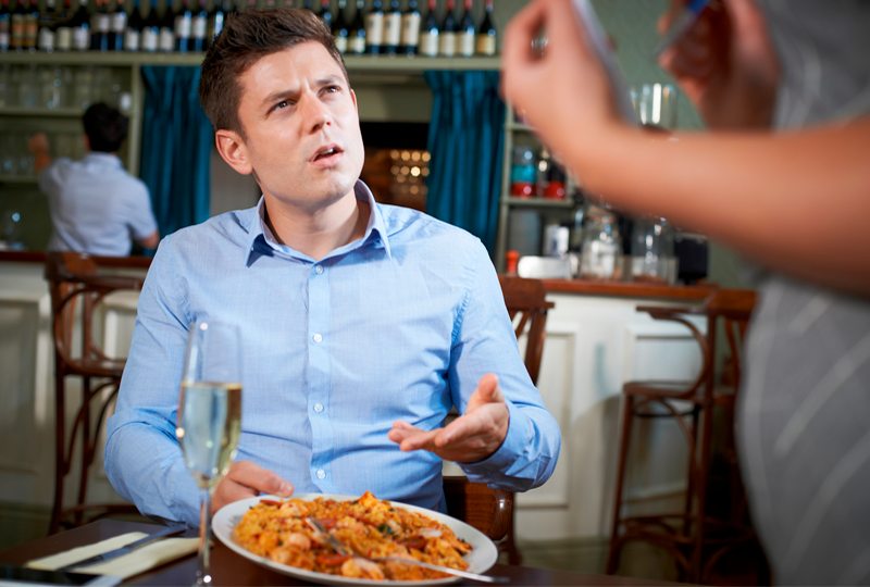 Cliente à mesa reclamando com o garçom durante o atendimento no salão
